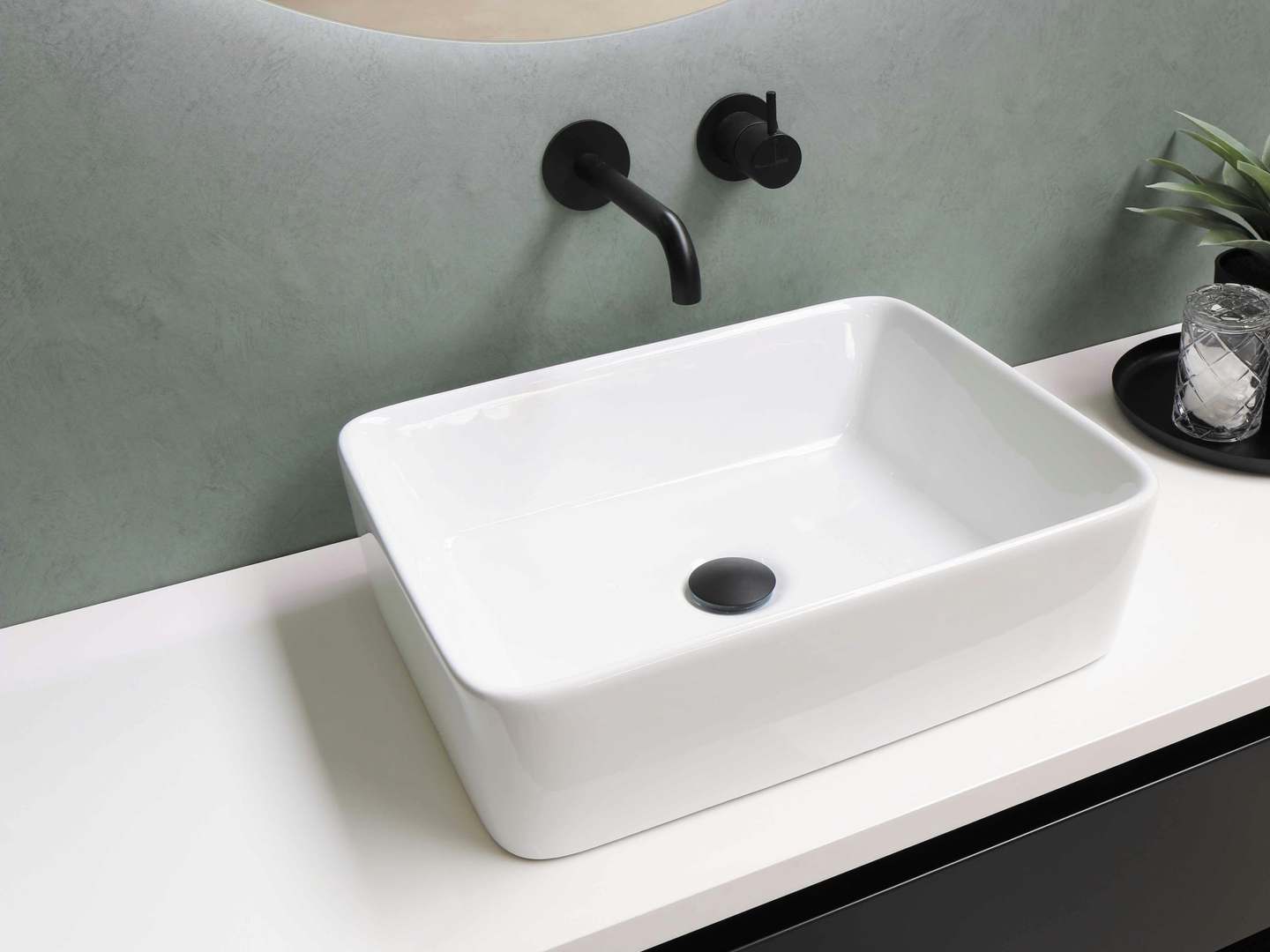 White rectangular basin on a white worktop with a matt black wall-mounted tap against a sage green wall