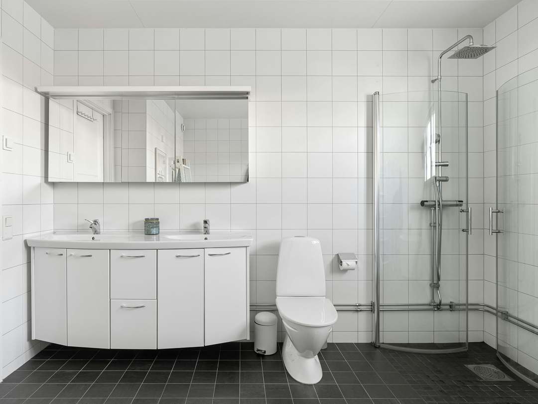 White-tiled bathroom with a double vanity unit, wall-hung toilet and a curved glass shower enclosure