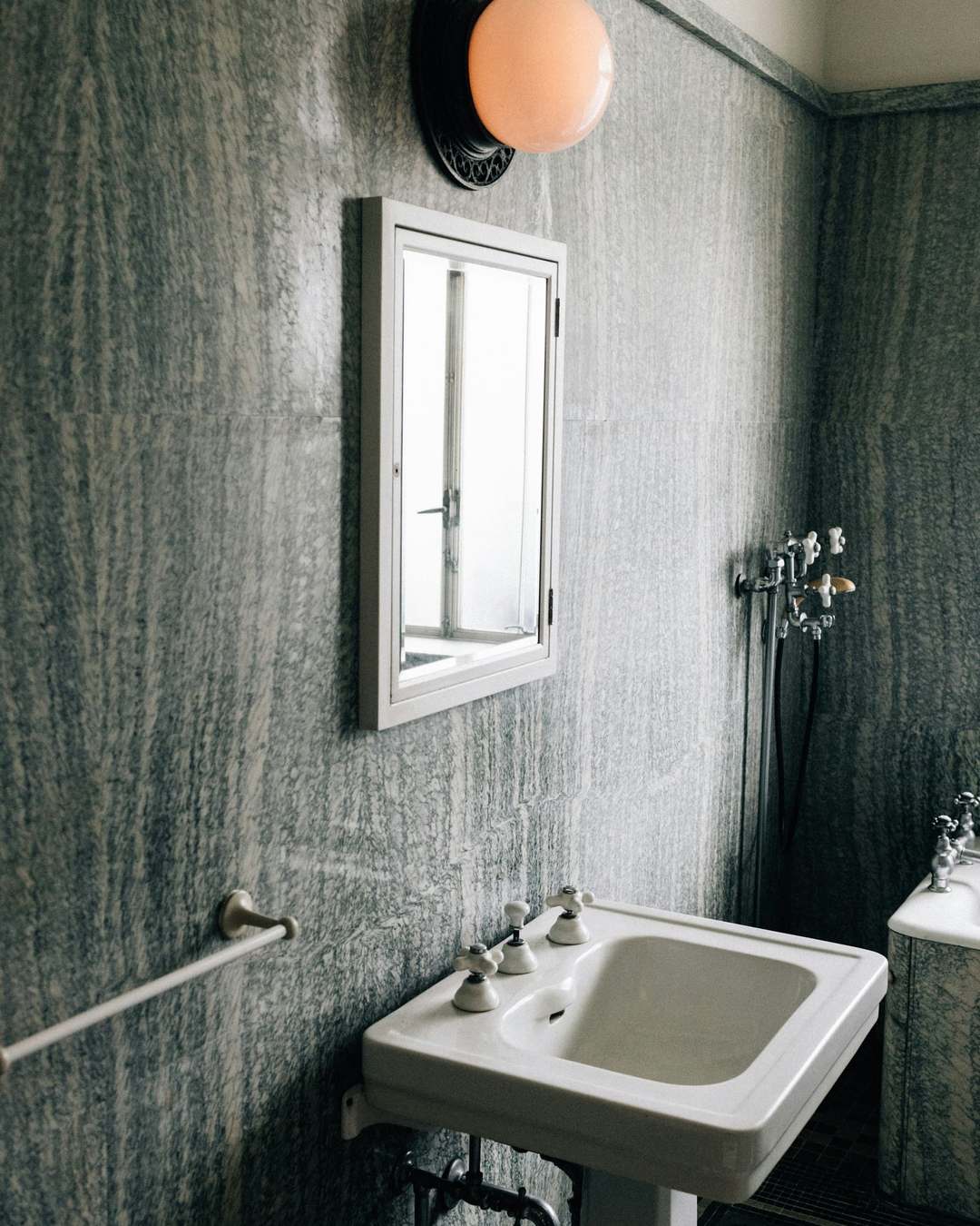 Period bathroom with veined stone walls, a pedestal basin with cross-head taps and a globe wall light