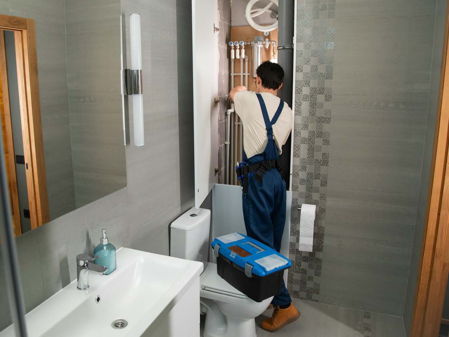 Plumber in overalls working on the pipework inside a bathroom service cupboard