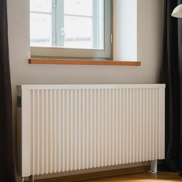 White vertical-fin radiator under a living room window, between dark curtains