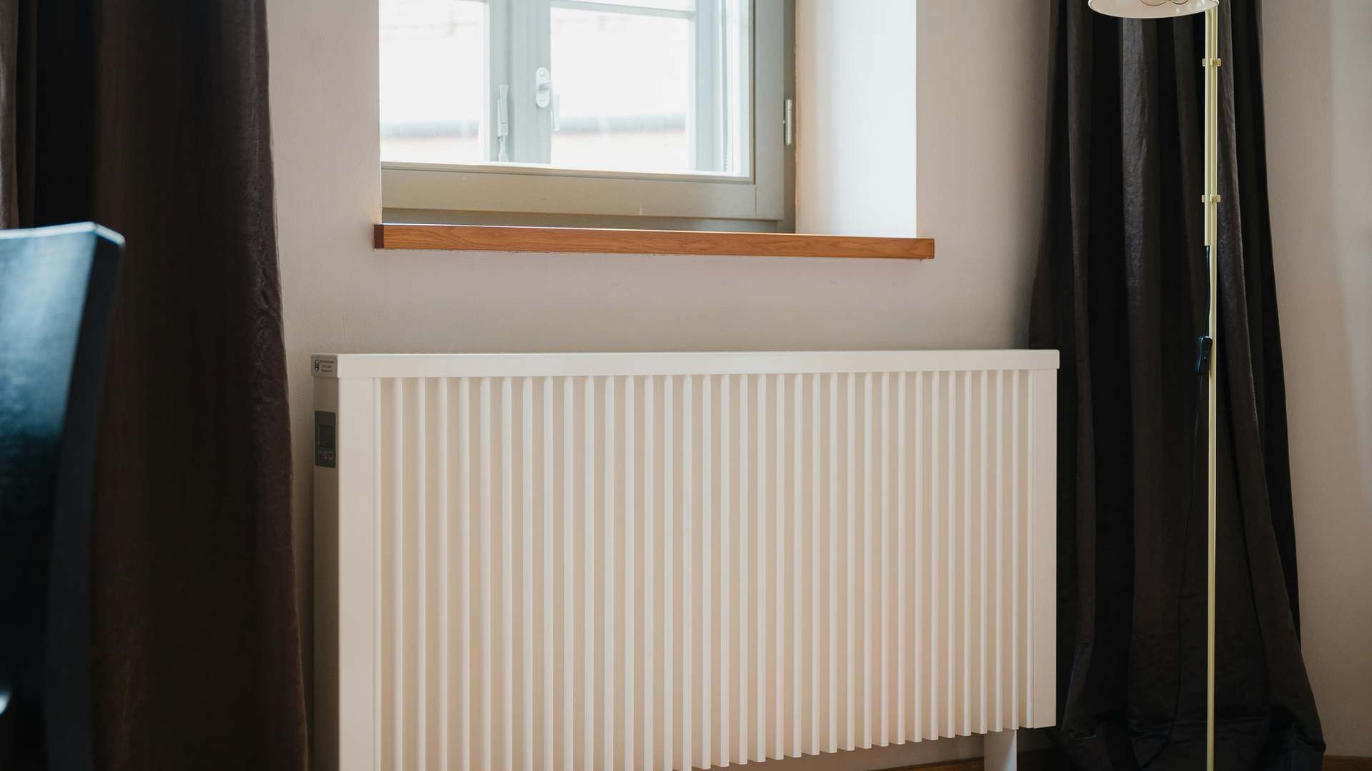 White vertical-fin radiator under a living room window, between dark curtains