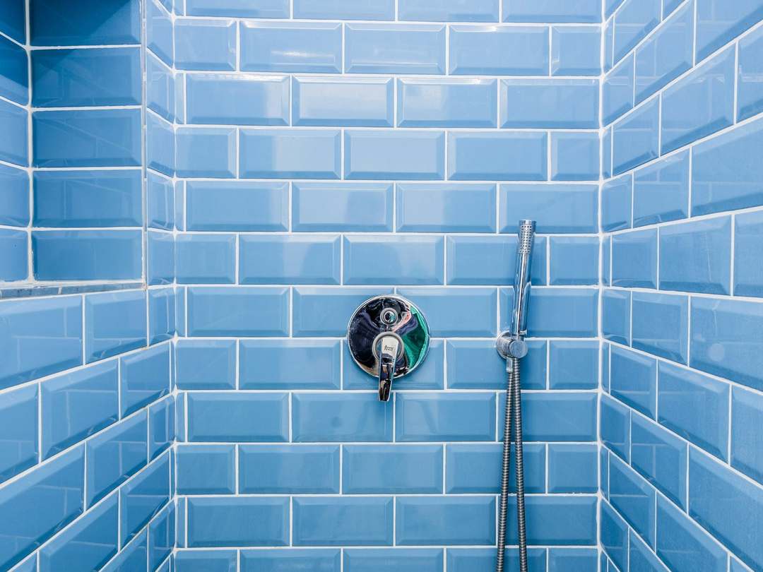 Shower wall in glossy blue metro tiles with a recessed shelf, chrome valve and hand shower