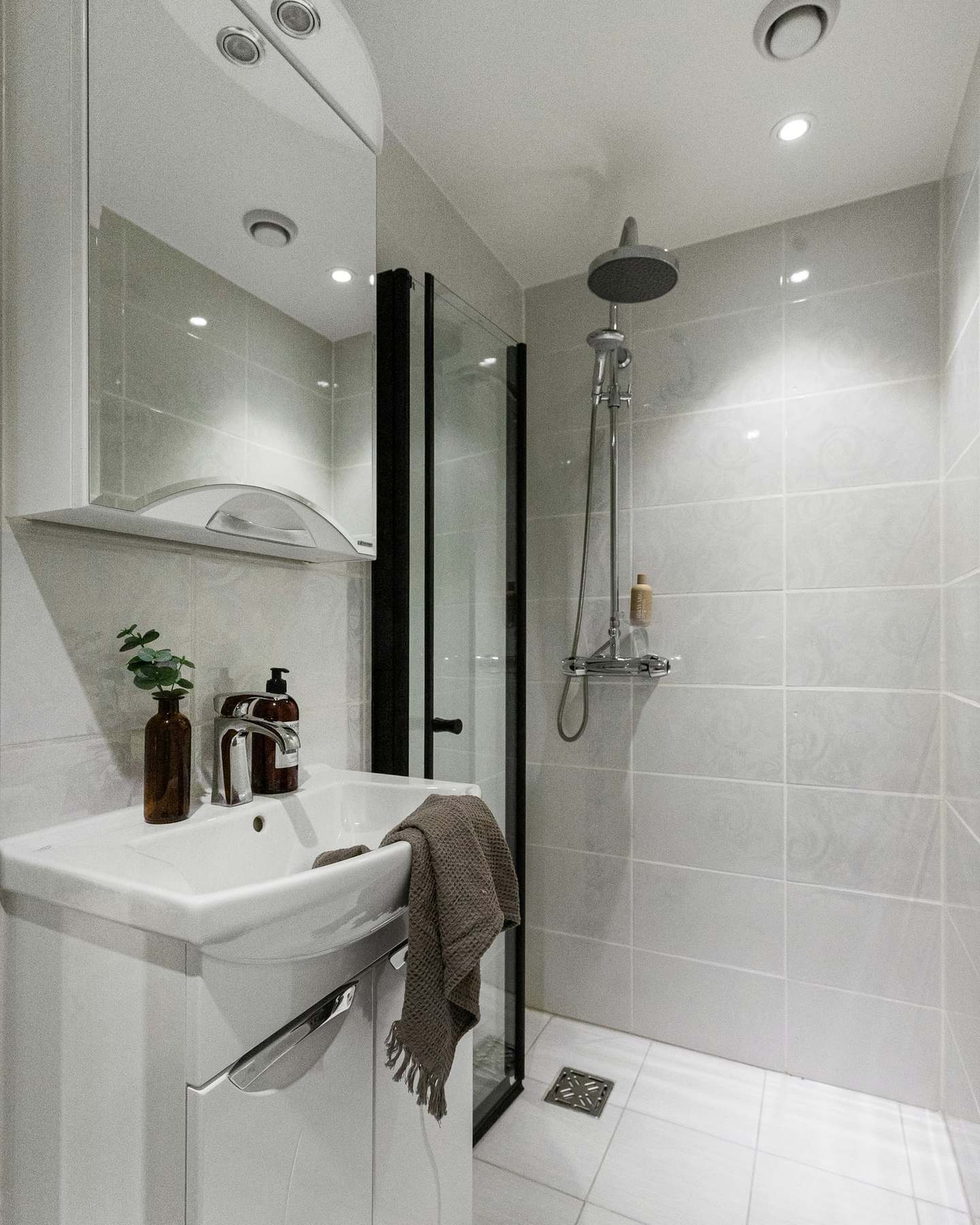 Compact shower room with large pale tiles, a black-framed glass screen and a thermostatic rainfall shower