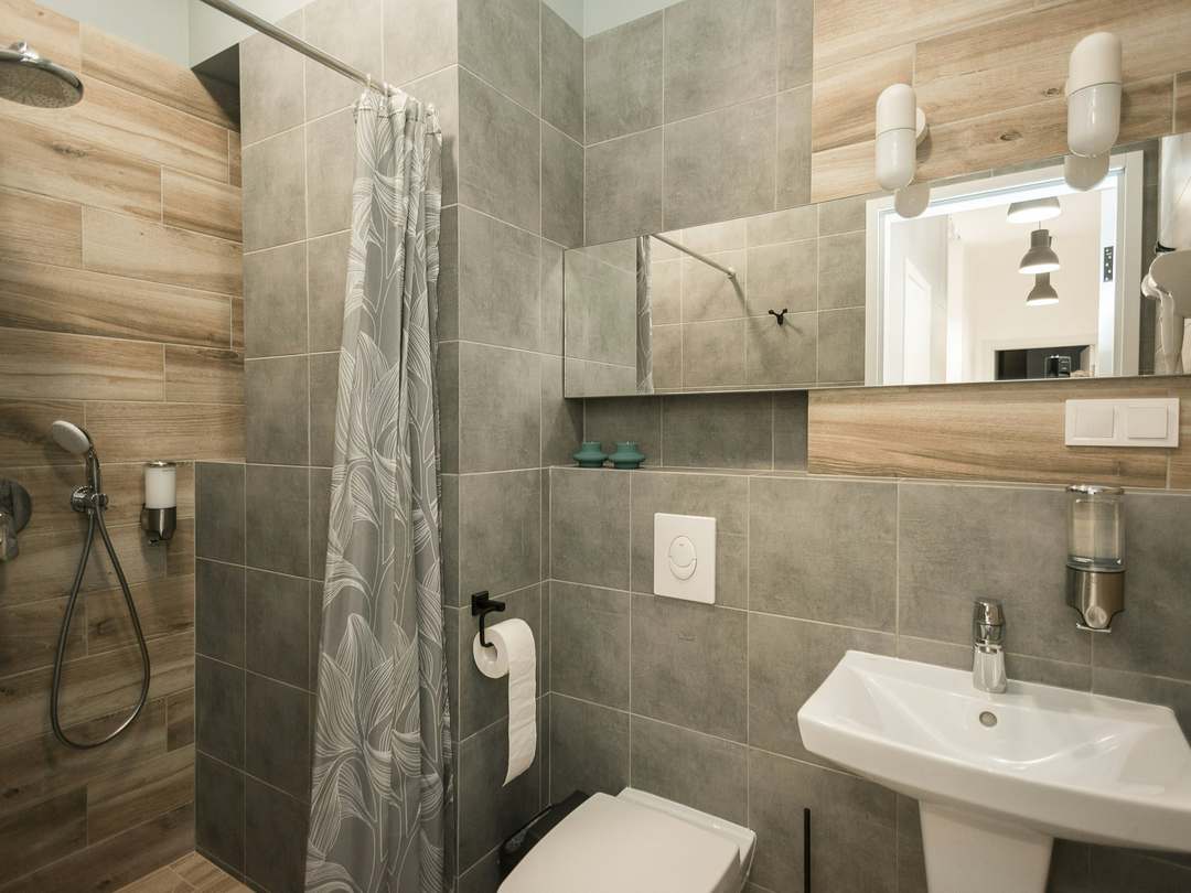 Small shower room with wood-effect and grey tiles, a pedestal basin and a wall-hung toilet