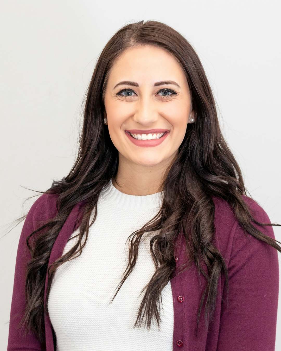 Smiling member of the office team in a burgundy cardigan, standing against a pale wall