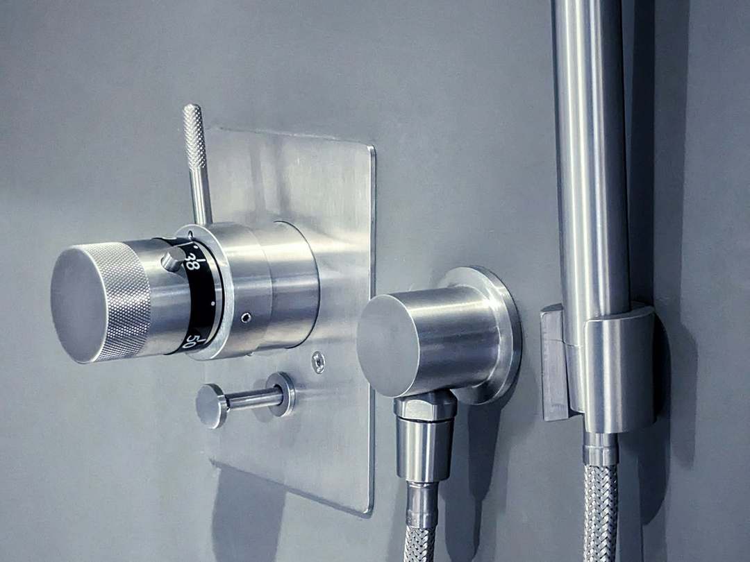 Brushed steel thermostatic shower valve and hand shower on a grey wall