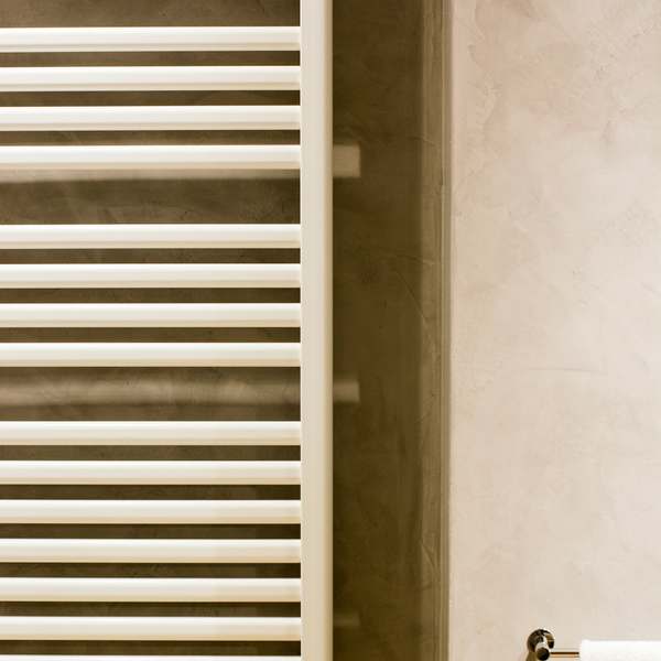 White ladder towel radiator on a polished plaster wall beside a towel rail