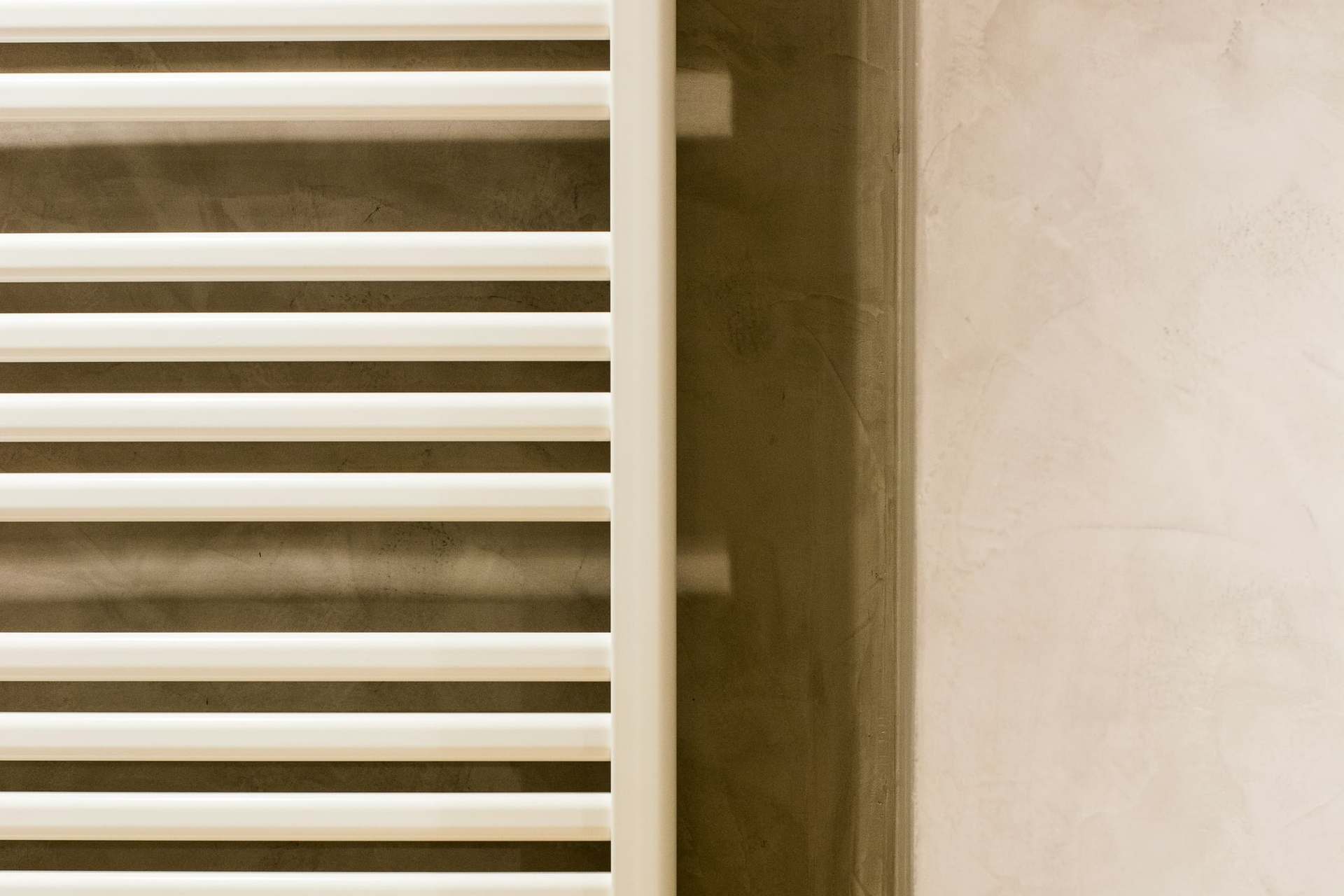 White ladder towel radiator on a polished plaster wall beside a towel rail